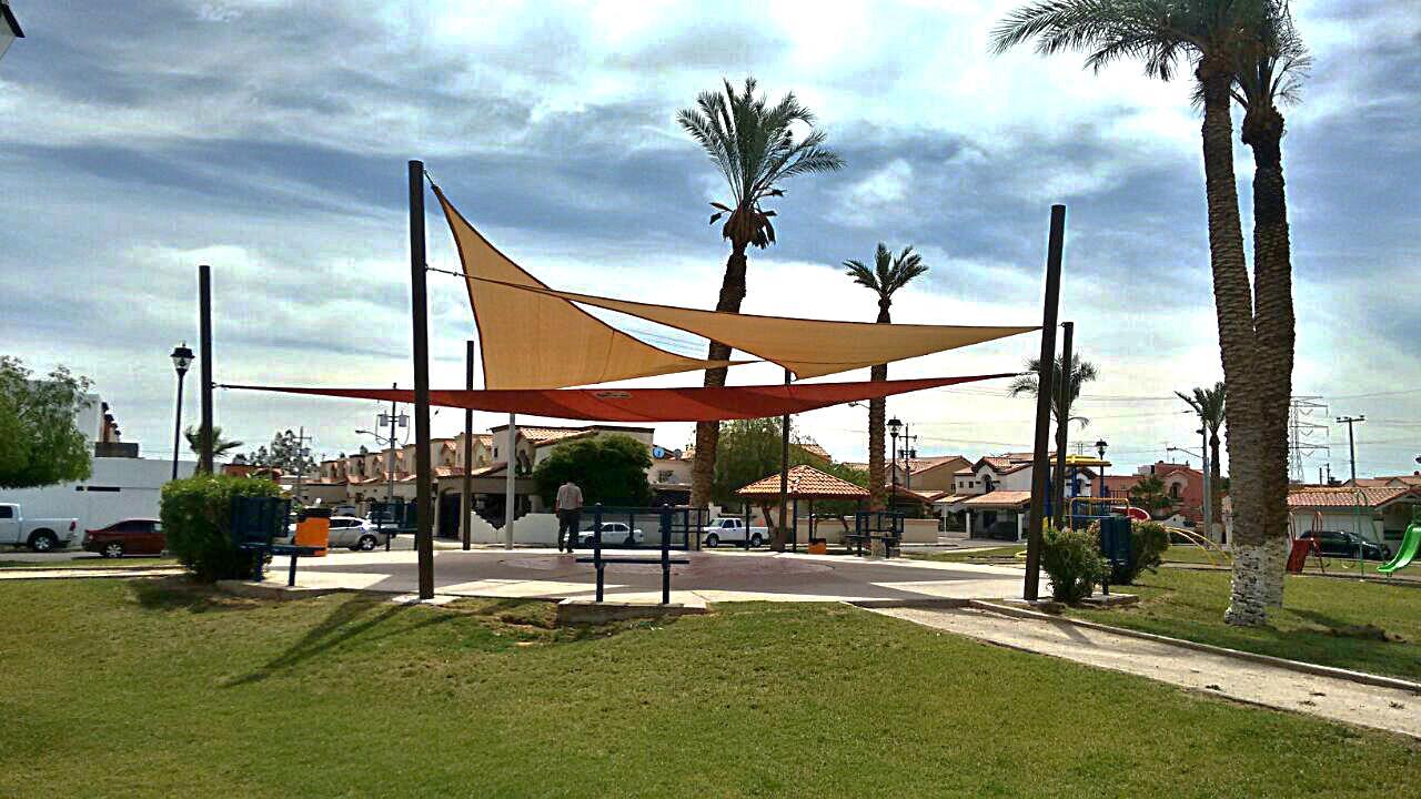 Velas triangulares de malla sombra en colores cálidos sobre un área pública
